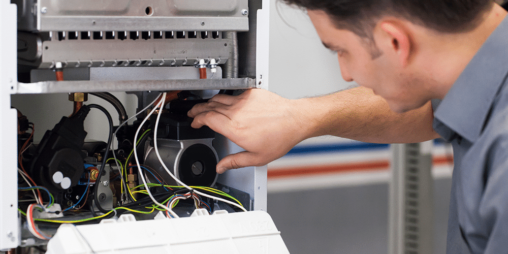 Male tech in gray shirt reaches into open furnace to replace a faulty part.