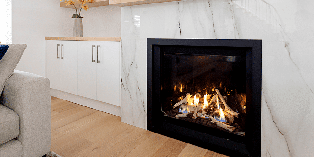 Best Type of Fireplace In-home fireplace set into a marble wall next to couch in living room.