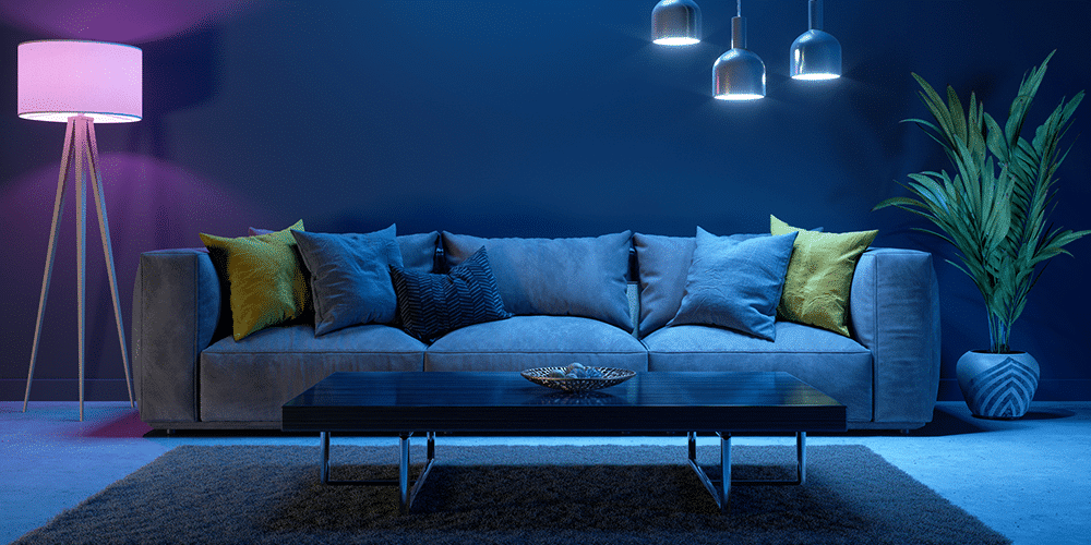 Image of a three-cushioned couch in a dark room lit by blue and purple lightbulbs.