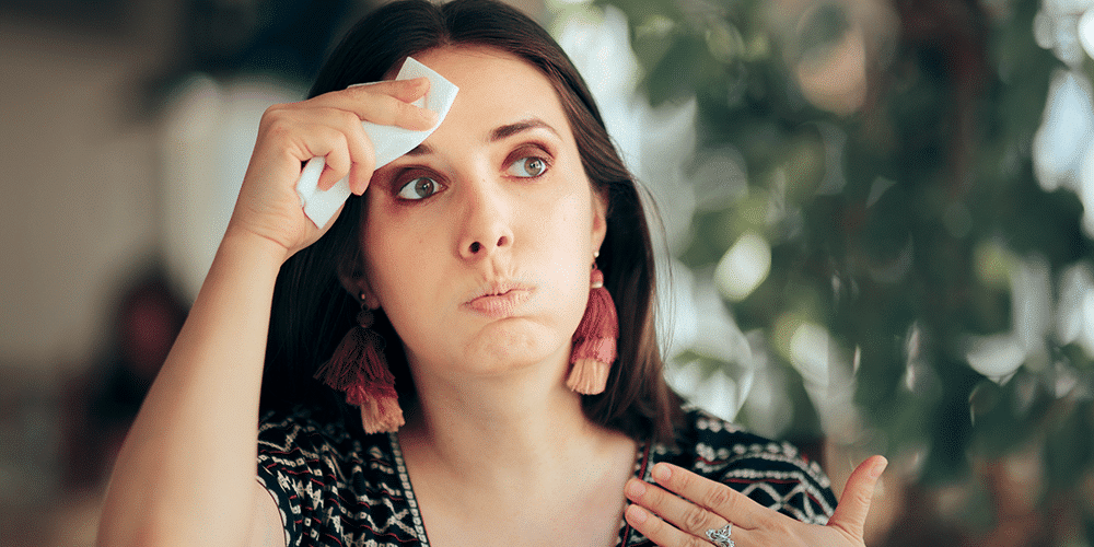 Female homeowner uses tissue to wipe forehead in house that’s too warm.