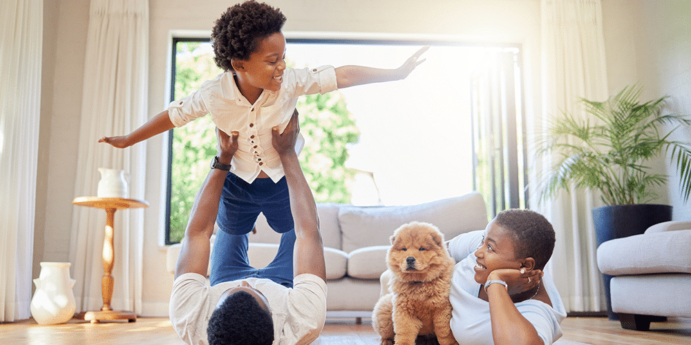Mom, dad, daughter, and dog lounge on floor in living room while father lifts up child.