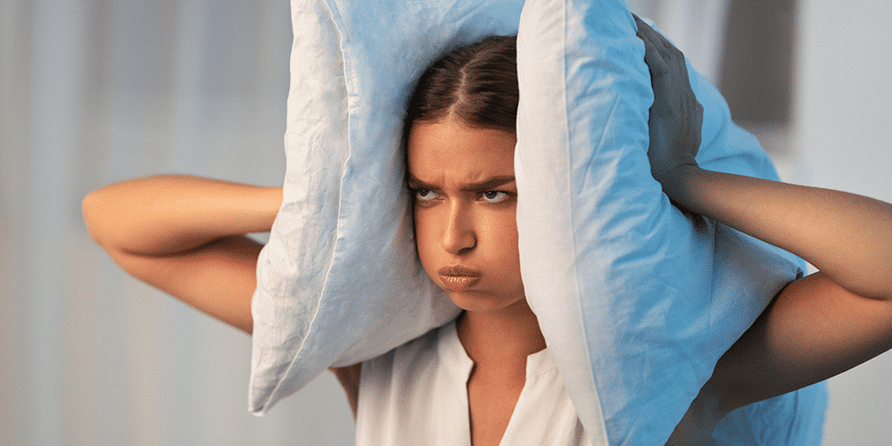 Frustrated female homeowner covers ears uses two pillows to cover her ears.