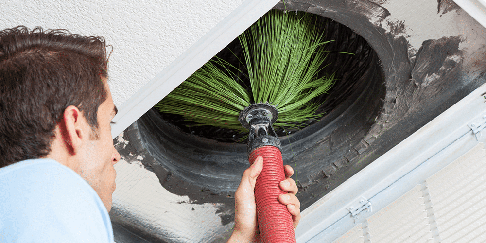 Air quality expert uses mechanical brush and hose to perform duct cleaning.