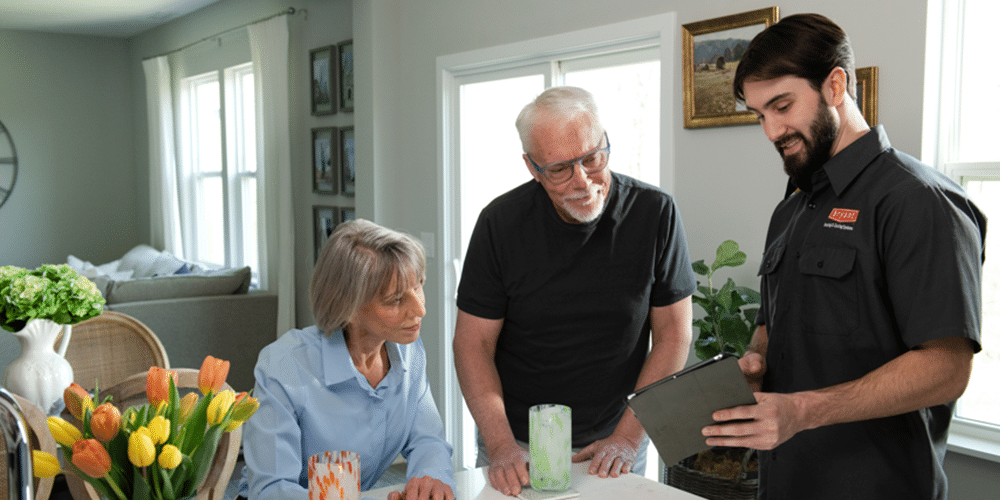 Purifier Tech in black shirt shows older homeowning couple purifier options on his tablet.