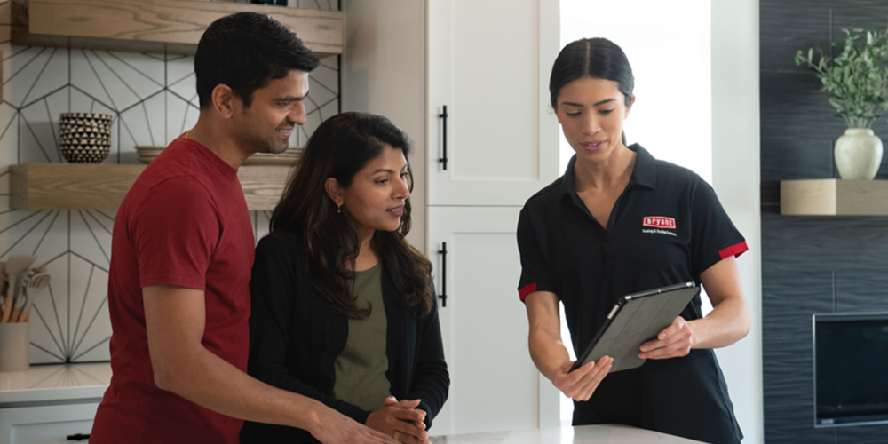 Female tech in black shirt shows homeowning couple the best furnace for their house.