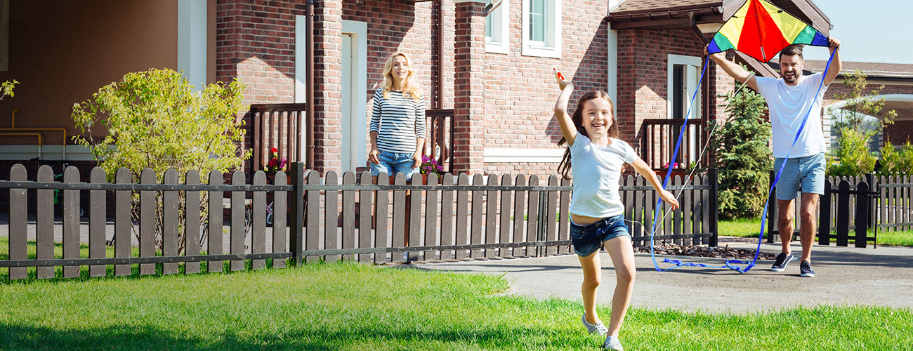 Family of three plays outside in front yard of home with a kite in the summertime.