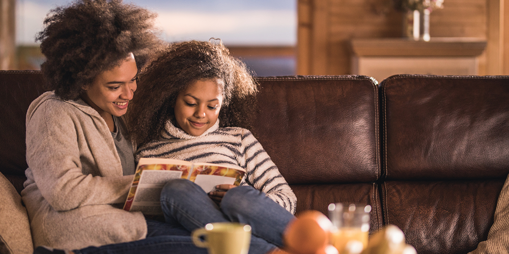 Mother and daughter snuggle on couch reading after learning how to keep your home warm.