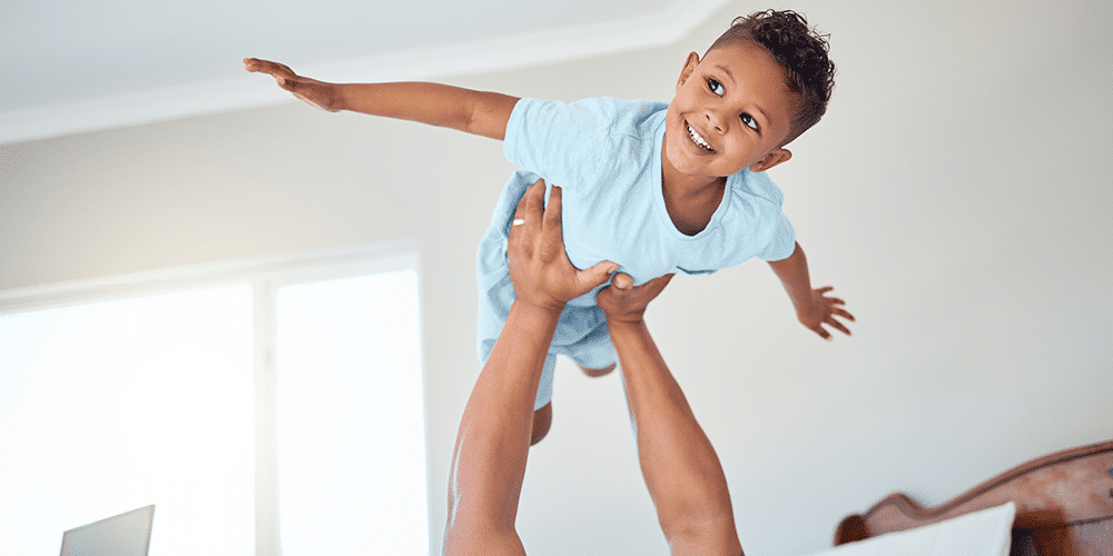 Improving Indoor Air Quality Little boy in blue shirt gets hoisted up like a superhero by his father in bedroom.