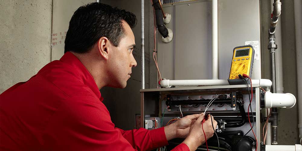 Male tech in red shirt connects tool during routine furnace maintenance.