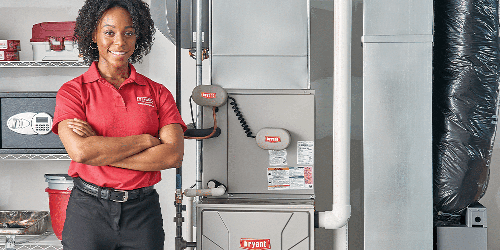Female tech in red shirt stands with arms crossed in front of new furnace.
