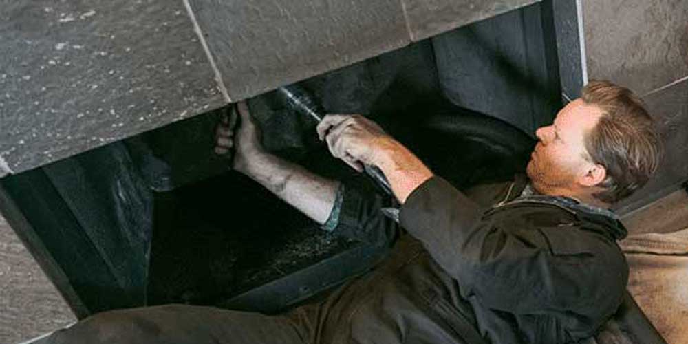 Tech in black jumpsuit performs fireplace maintenance for homeowner.