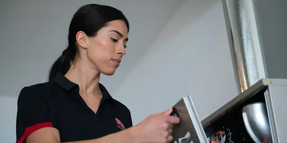 Female tech opens front of heating system to perform furnace tune-up.
